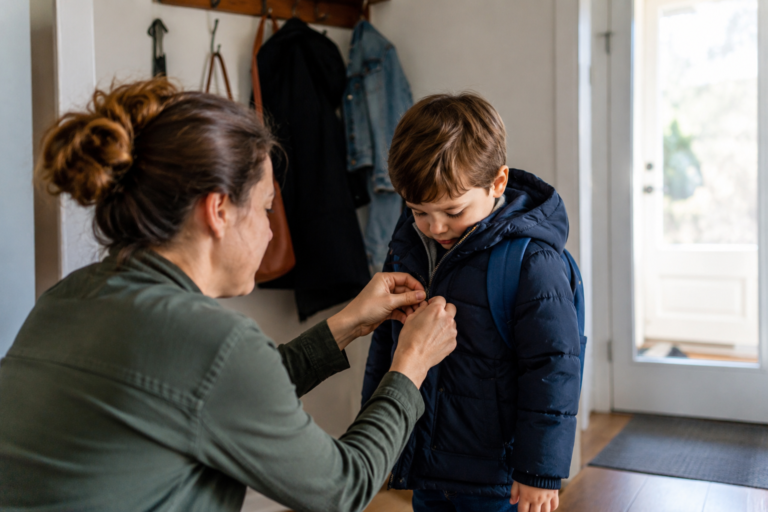 Une mère aide son enfant à fermer son manteau, illustration de la surprotection parentale et de l’apprentissage de l’autonomie.