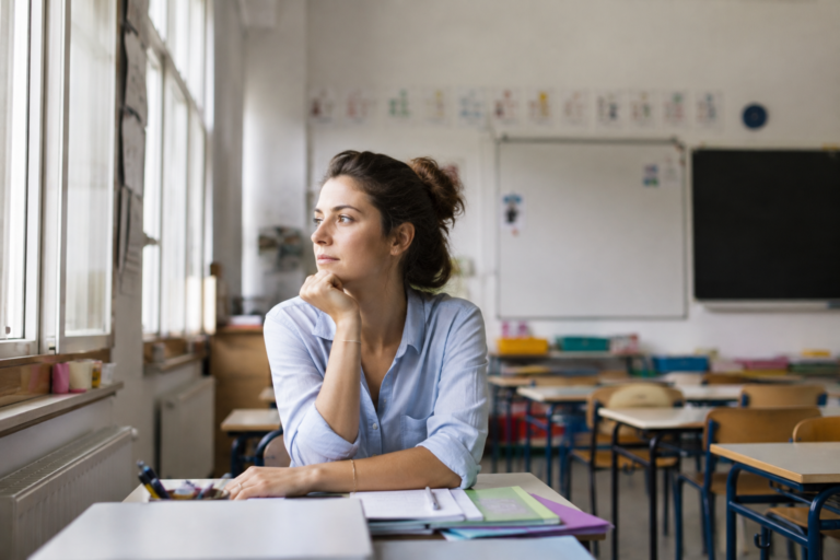 Rentrée scolaire enseignants : une enseignante pensive dans sa classe vide avant l’arrivée des élèves.